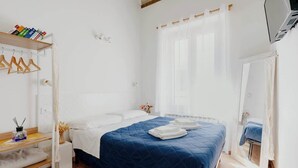 A bedroom with a bed, a bedside table, a hanging wardrobe, and a window with curtains.