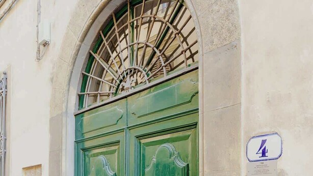 A green double door with ornate handles, a metal grille above, and a plaque on the wall to the right.