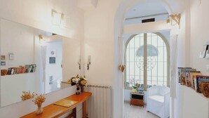 A hallway with a wooden bench, a mirror, a radiator, a white chair, and a window with a view of the outside.