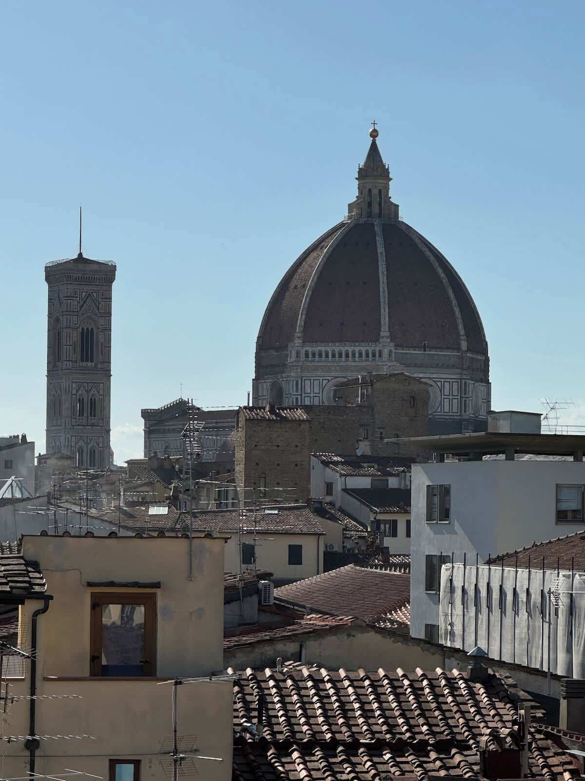 A cityscape with a prominent dome and a tower, surrounded by buildings with terracotta roofs.