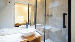 Une salle de bain moderne avec un grand miroir, un meuble-lavabo en bois, un lavabo blanc et une douche séparée par une paroi en verre.