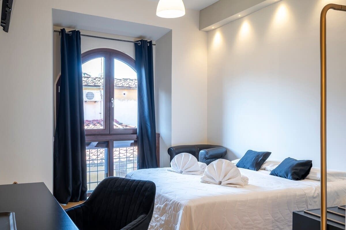 Une chambre d’hôtel avec un lit, un bureau, une chaise et une grande fenêtre avec des rideaux.