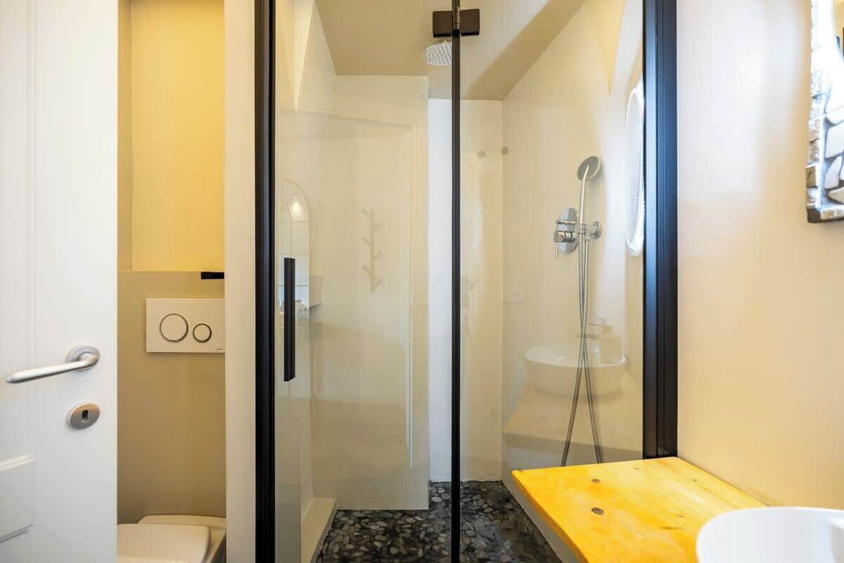 A modern bathroom with a glass shower enclosure, a wooden bench, and a toilet.