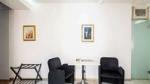 Une pièce avec une table blanche, deux chaises noires, un étendoir métallique et deux tableaux encadrés accrochés aux murs.