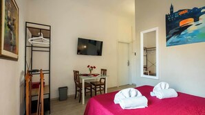 A hotel room with a bed, a desk with a chair, a TV, a painting, and a wardrobe.