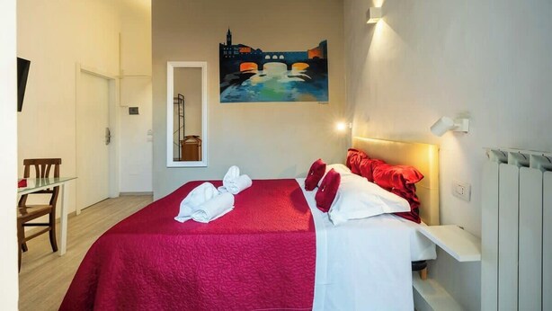 A hotel room with a bed, a painting on the wall, and a desk with a chair.