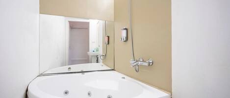 Un baño con una bañera grande, un cabezal de ducha en la pared y un espejo que refleja la habitación.
