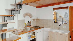 A kitchen with wooden countertops, a built-in stove, and a sink. There is a small window with a view of a staircase and a stone wall.
