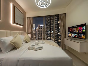 A hotel room with a bed, a TV, and a view of high-rise buildings.