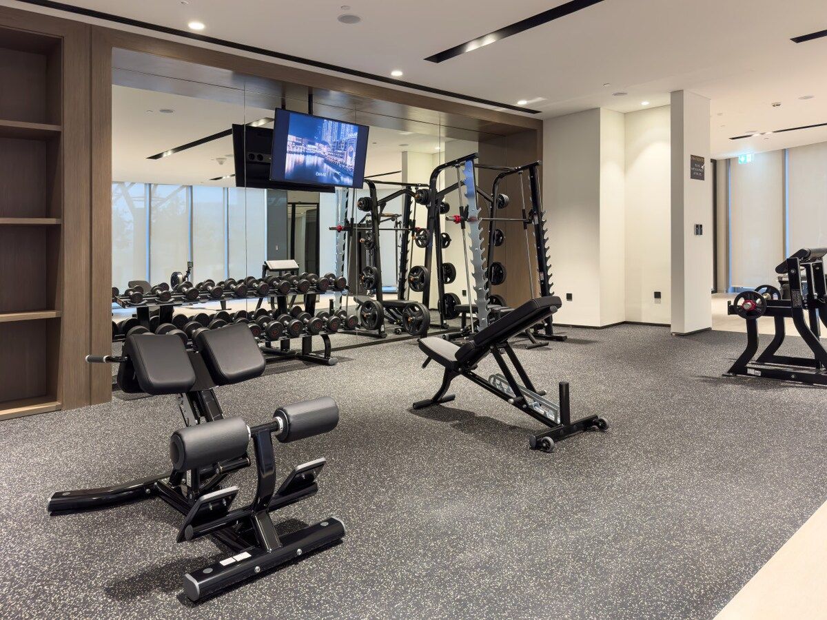 A gym with various exercise equipment, including dumbbells, weight machines, and a television screen.