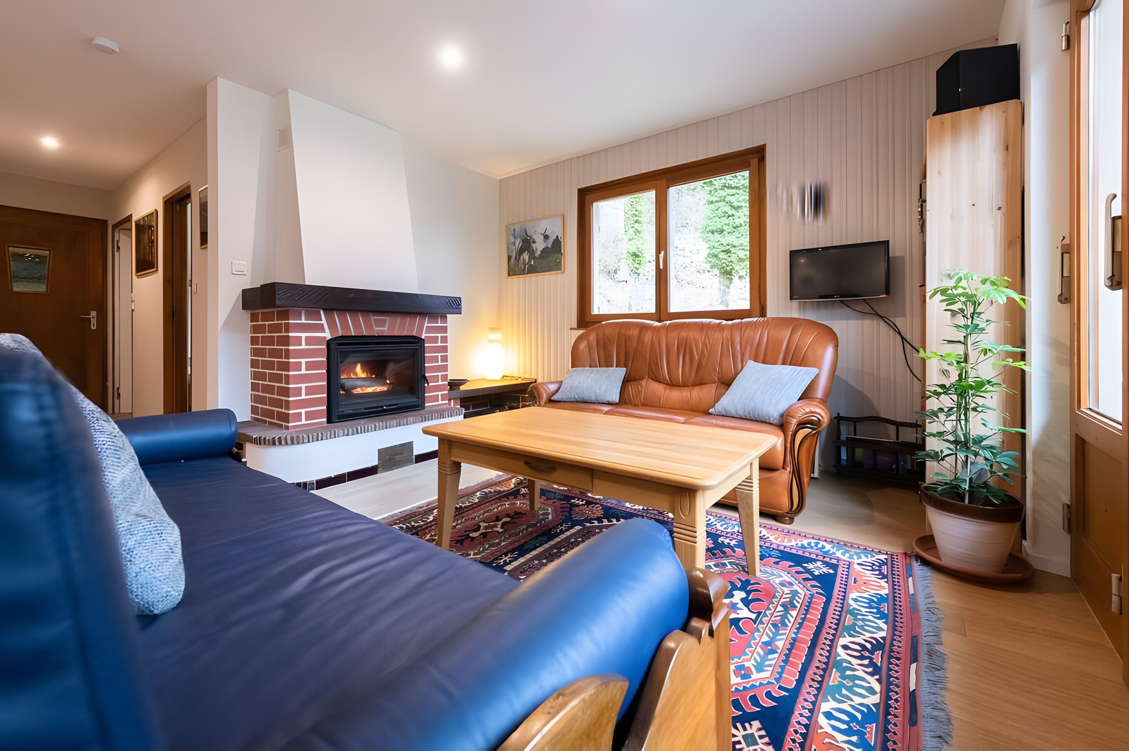 Una sala de estar con chimenea, sofá de cuero, mesa de centro de madera y un ventanal grande.