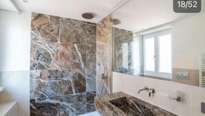 A modern bathroom with a large mirror, a marble sink, and a shower area with marble tiles. - Victoria rooms  (Rome)