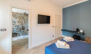 A modern hotel room with a large bed, a flat-screen TV, a stone wall, and a blue accent wall. - Victoria rooms  (Rome)