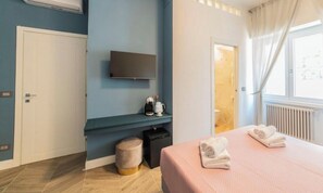 A modern hotel room with a flat-screen TV, a small seating area with a coffee machine, a bed with towels, and a window with curtains. - Victoria rooms  (Rome)
