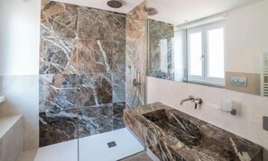 A modern bathroom with a large mirror, a marble sink, and a shower area with marble tiles. - Victoria rooms  (Rome)