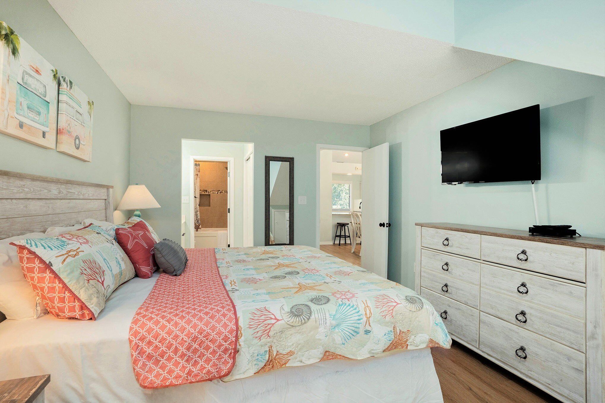A bedroom with a bed, a dresser, a TV, and a door leading to another room.
