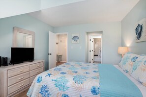 A bedroom with a bed, dresser, TV, and artwork on the walls.