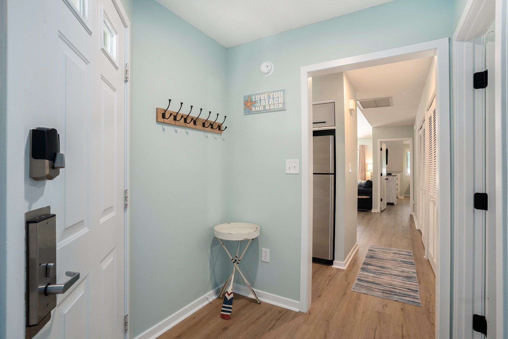 A hallway with a coat rack, a small sink, and a refrigerator in the background.