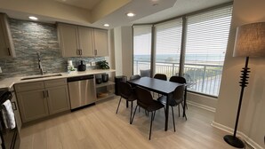 A modern kitchen with a dining area, large windows with blinds, and a view of the outdoors. - 504 Brighton 2 Bedroom Condo (Myrtle Beach)