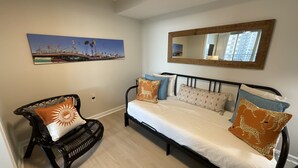 A bedroom with a bed, a chair, a wall-mounted mirror, and a picture. - 504 Brighton 2 Bedroom Condo (Myrtle Beach)