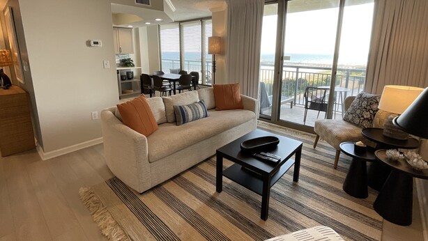 A modern living room with a sofa, coffee table, and a view of the balcony. - 504 Brighton 2 Bedroom Condo (Myrtle Beach)