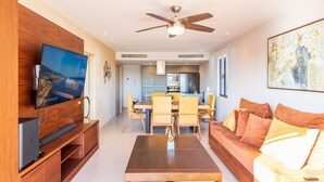 A modern living room with a flat-screen TV, wooden furniture, a dining area, and a kitchen in the background. - D410 Lorena Ochoa 4 Bedroom Apts (Playa del Carmen)