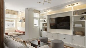 A modern living room with a large flat-screen TV, built-in shelving, and a cozy seating area. - Charming Family Retreat – 4BR Marylebone (Greater London)