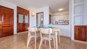 A dining area with a wooden table and chairs, a kitchen in the background, and a tiled floor. - El Charcón B • 10 meters to the beach • LVH (Arrieta)