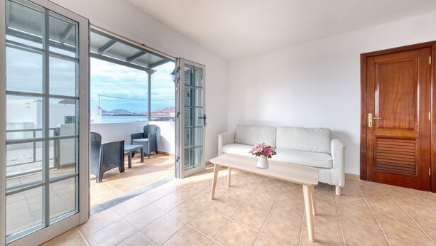 A spacious living area with a sliding glass door leading to a balcony, a white sofa, a wooden coffee table, and a view of the sea. - El Charcón B • 10 meters to the beach • LVH (Arrieta)