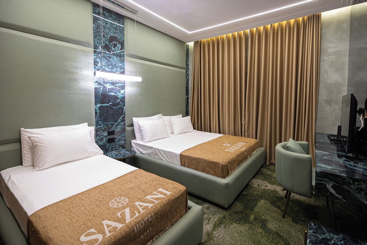 Hotellihuone, jossa on kaksi sänkyä, työpöytä, tuoli ja suuri ikkuna, jossa on verhot.