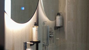 A bathroom with a marble sink, a round mirror, and a towel dispenser. - Sazani Hotel (Vlorë)