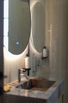 Un baño con lavamanos de mármol, un espejo redondo y un dispensador de toallas.