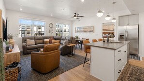 A modern living room with a sofa, a coffee table, and a dining area with chairs. There is a kitchen with a refrigerator and a dining table. - Mane Stay At Terra 3 Bedroom Condo (Hurricane)