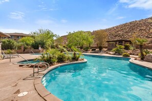 Ein Pool mit geschwungener Form, umgeben von viel Grün und einer hügeligen Landschaft.