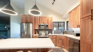 A modern kitchen with wooden cabinets, stainless steel appliances, a central island, and pendant lighting. - Stylish 4BR Canyons Village-Walk to Cabriolet-Hidden Creek 37D (Park City)