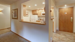 A hallway leading to a kitchen with wooden cabinets, a refrigerator, and a microwave.