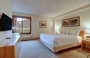 A bedroom with a large bed, a desk with a TV, a window with a mountain view, and a framed picture on the wall. - Vs453 Village Square 1 Br 1 Ba 1 Bedroom Condo (Copper Mountain)