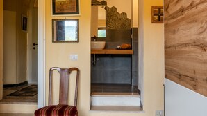 Ein Flur mit einem Holzstuhl, einer Treppe, die zu einem Badezimmer führt, und gerahmten Bildern an den Wänden.