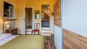 Ein Schlafzimmer mit einem Bett, einem Holzschrank, einem Sessel, einer Heizung und einer Treppe zu einem Badezimmer.
