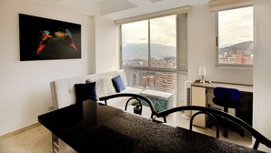 A modern apartment with a city view, a large window, a white sofa, a desk, and a colorful painting. - Apartamentos Oslo-by Medellin Experience (Medellin)