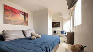 A bedroom with a large bed, a desk, and a chair. There is a painting on the wall and a window with blinds. - Apartamentos Oslo-by Medellin Experience (Medellin)