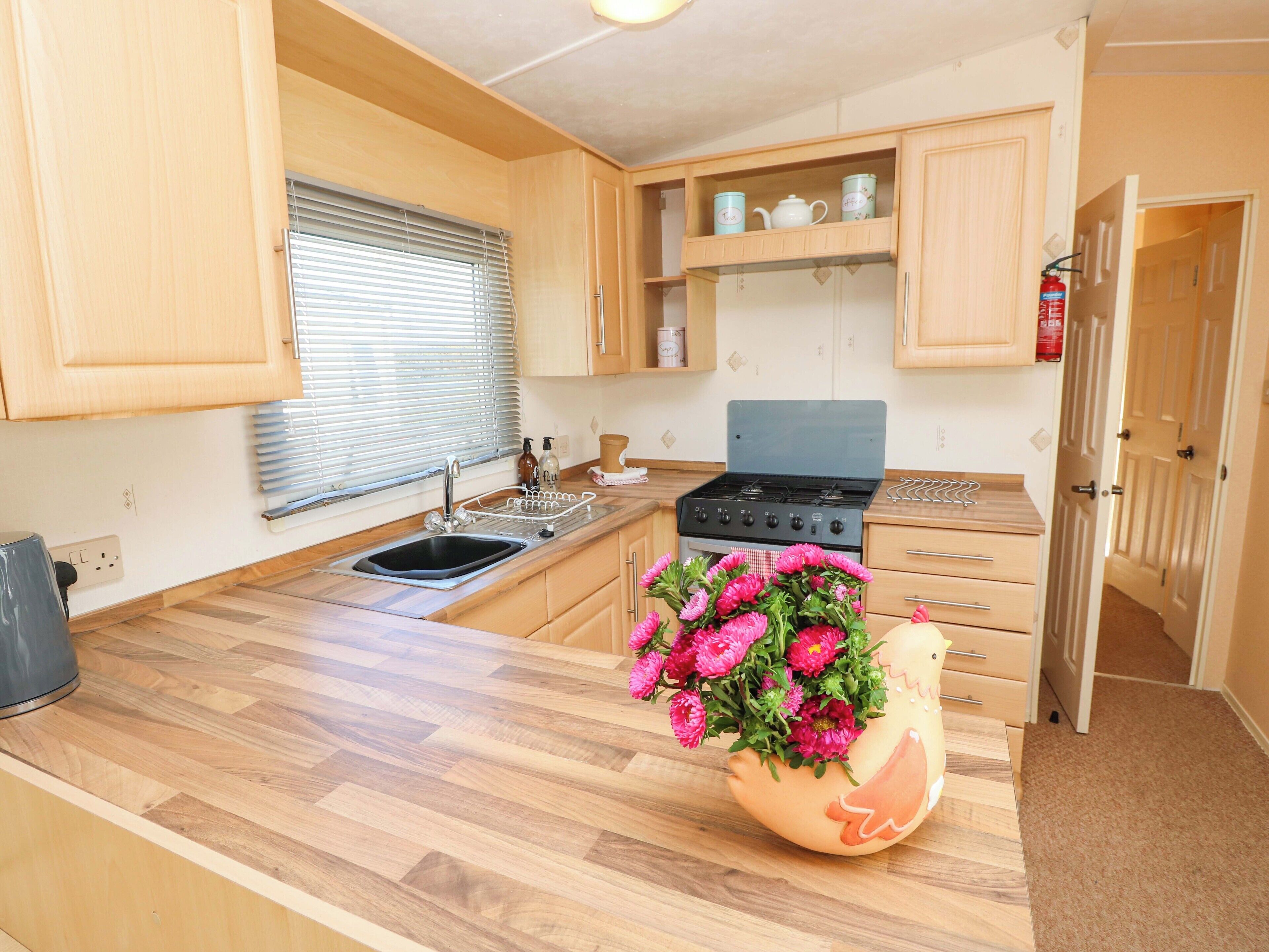 A compact kitchen with wooden cabinets, a sink, a stove, and a decorative flower vase.
