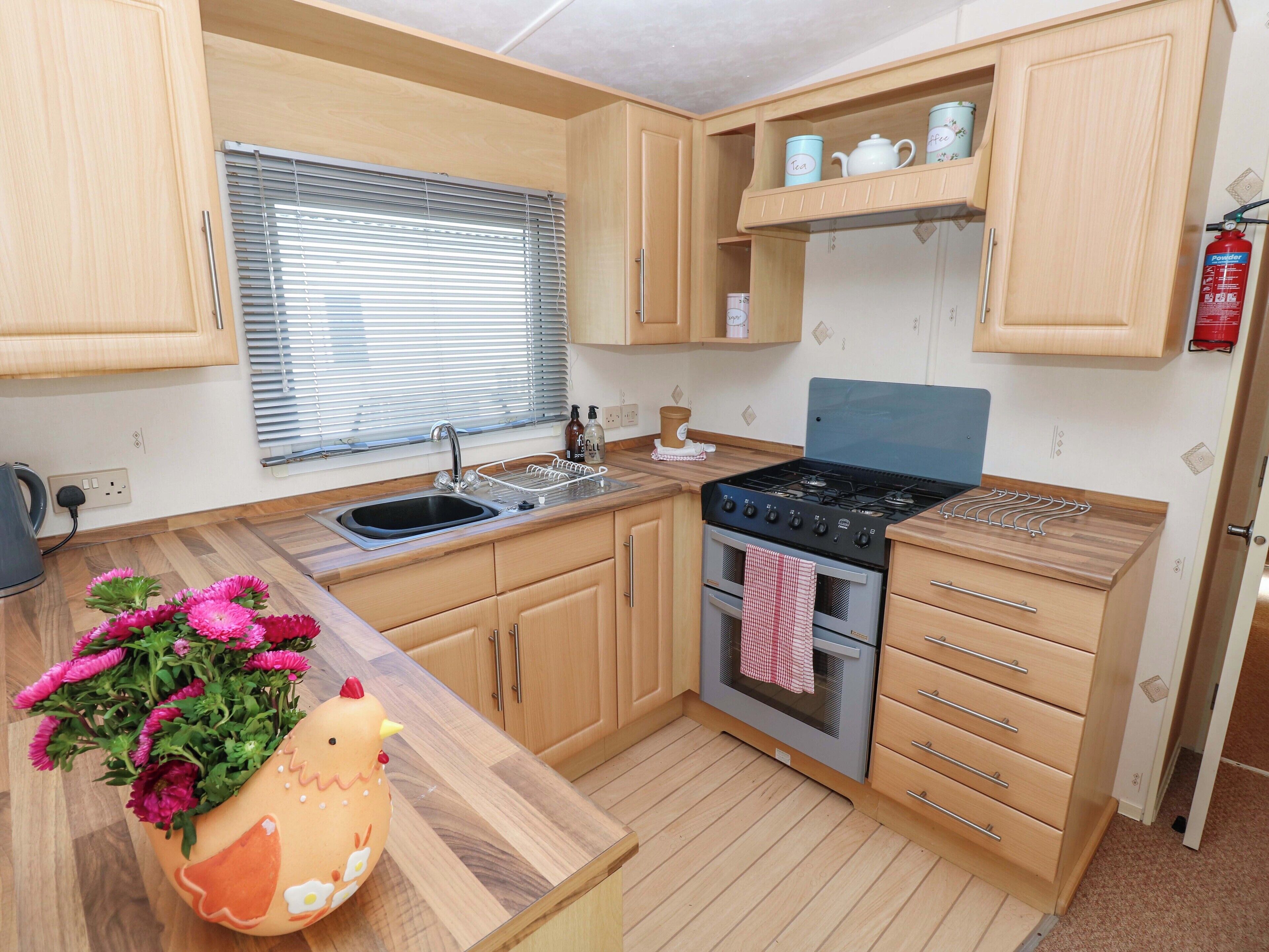 A compact kitchen with wooden cabinets, a gas stove, a sink, and a window with blinds.