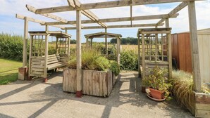Une structure de pergola en bois, agrémentée de bancs et de jardinières, installée dans un jardin avec un chemin de gravier.
