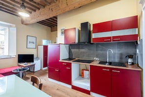 Cocina compacta con armarios rojos, estufa negra y una pequeña zona de comedor con mesa y sillas rojas.