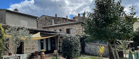 Ein rustikales Steinhaus mit Terrasse, Sitzgelegenheiten im Freien und einem Garten mit verschiedenen Pflanzen und Blumen.