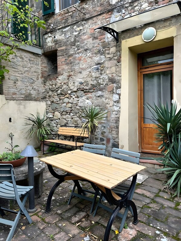 An outdoor patio with a wooden table and chairs, surrounded by potted plants and a stone wall. - 'Arco - Antiche Dimore' with Shared Pool, Wi-Fi and Air Conditioning (Siena)