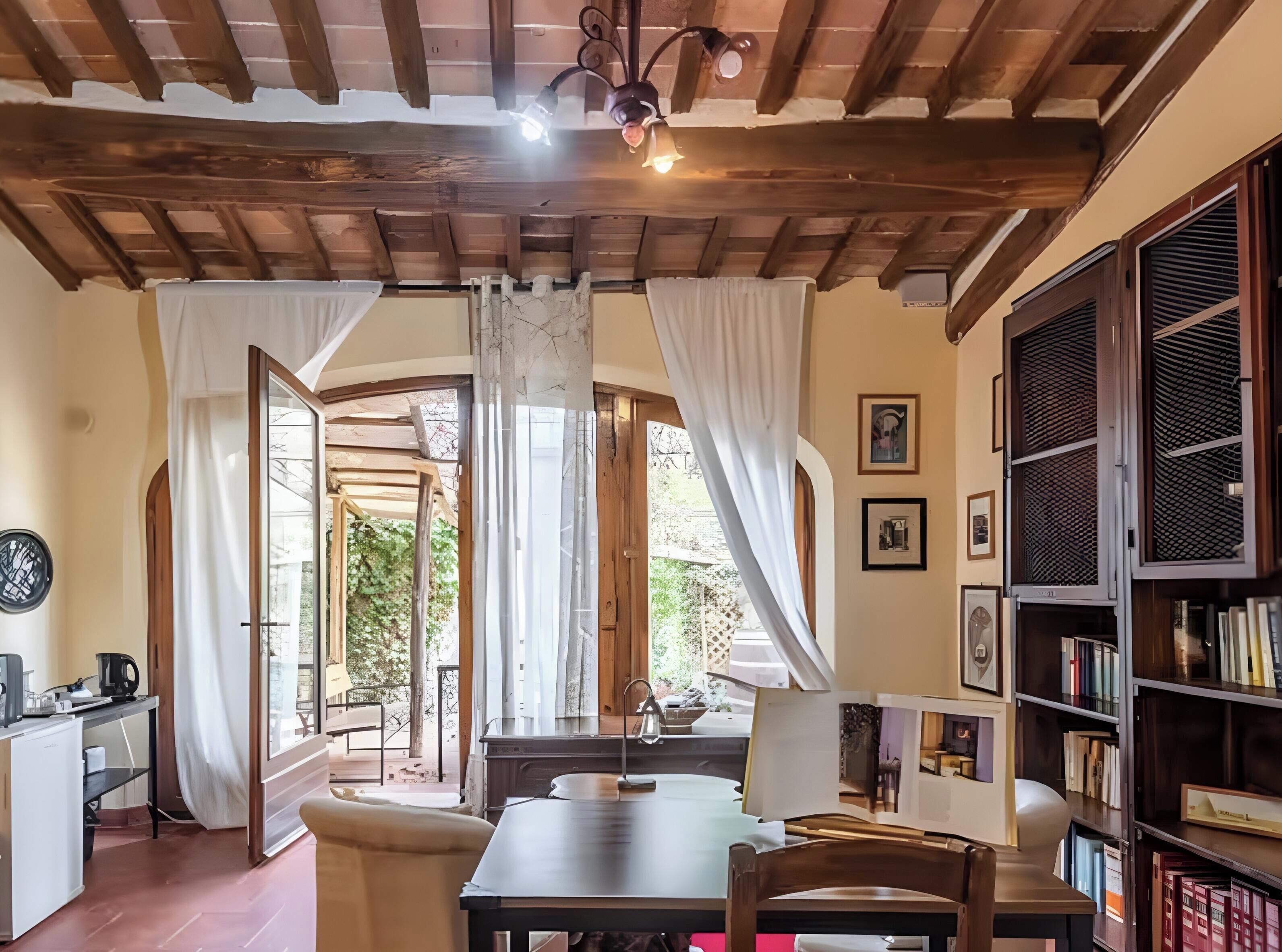 Una habitación acogedora con techo de madera, una mesa de comedor, una estantería y vistas al exterior.