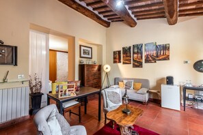 Un salon chaleureux avec un canapé, une table basse en bois, une table à manger et un réfrigérateur. Des tableaux encadrés ornent le mur et une lampe est posée sur une table d’appoint.