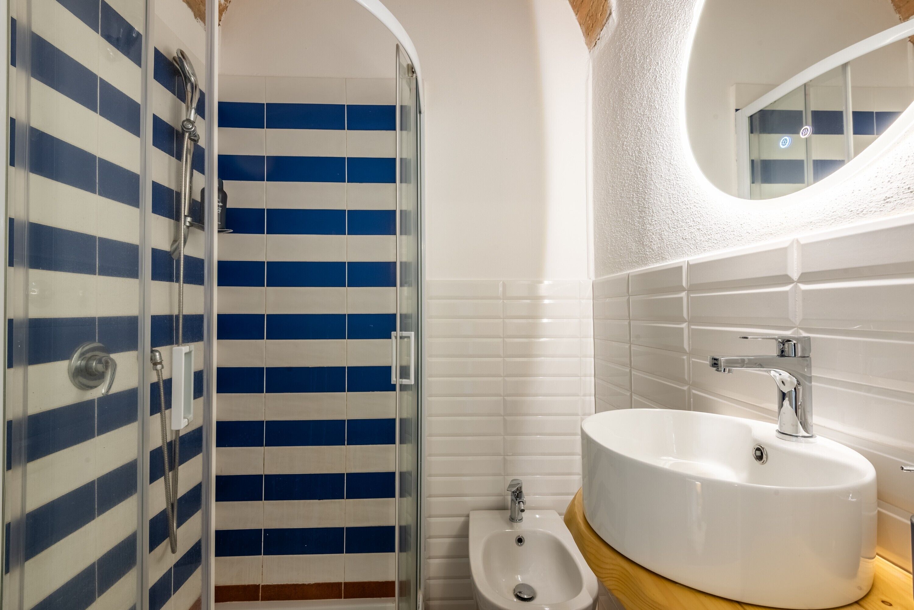 A bathroom with a glass shower enclosure, a bidet, and a sink with a mirror above it.